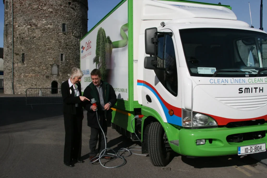 Two people inspecting a charger next to an electric truck. 