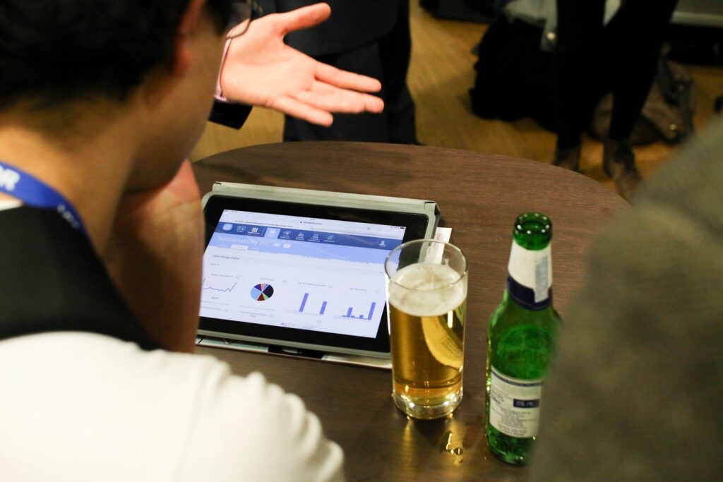 A person looks at a tablet device showing various graphs, placed next to a glass of beer. 