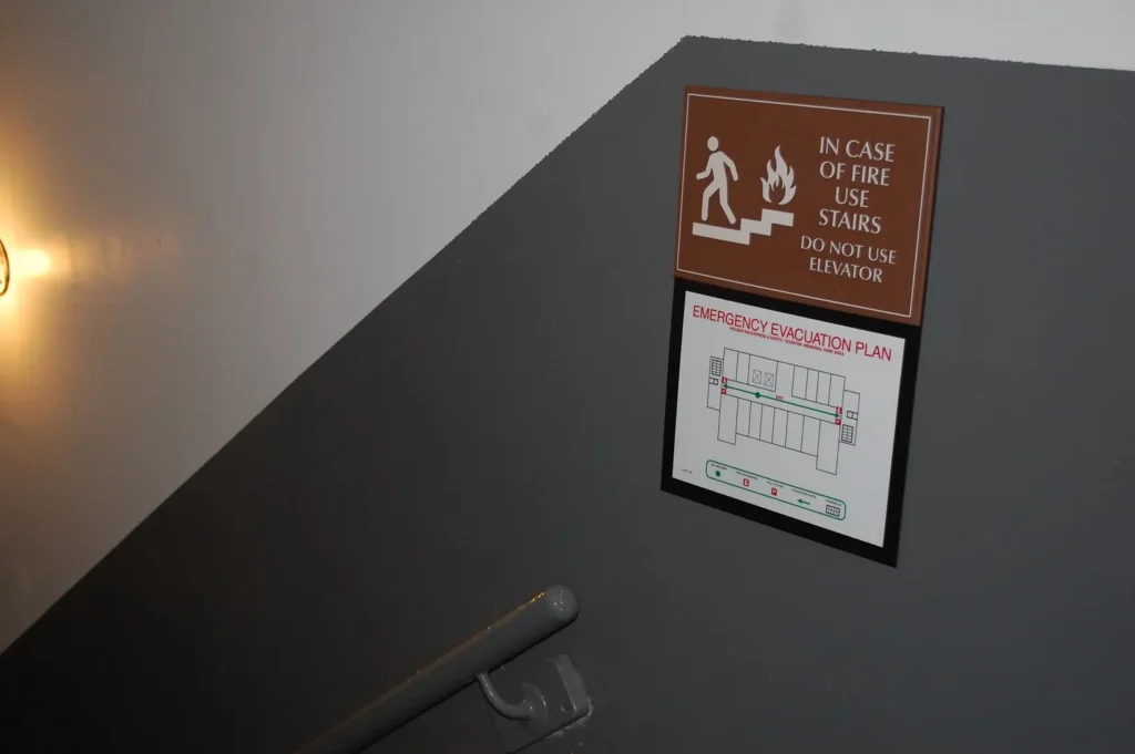 A fire emergency exit sign above an evacuation map near a stairway.