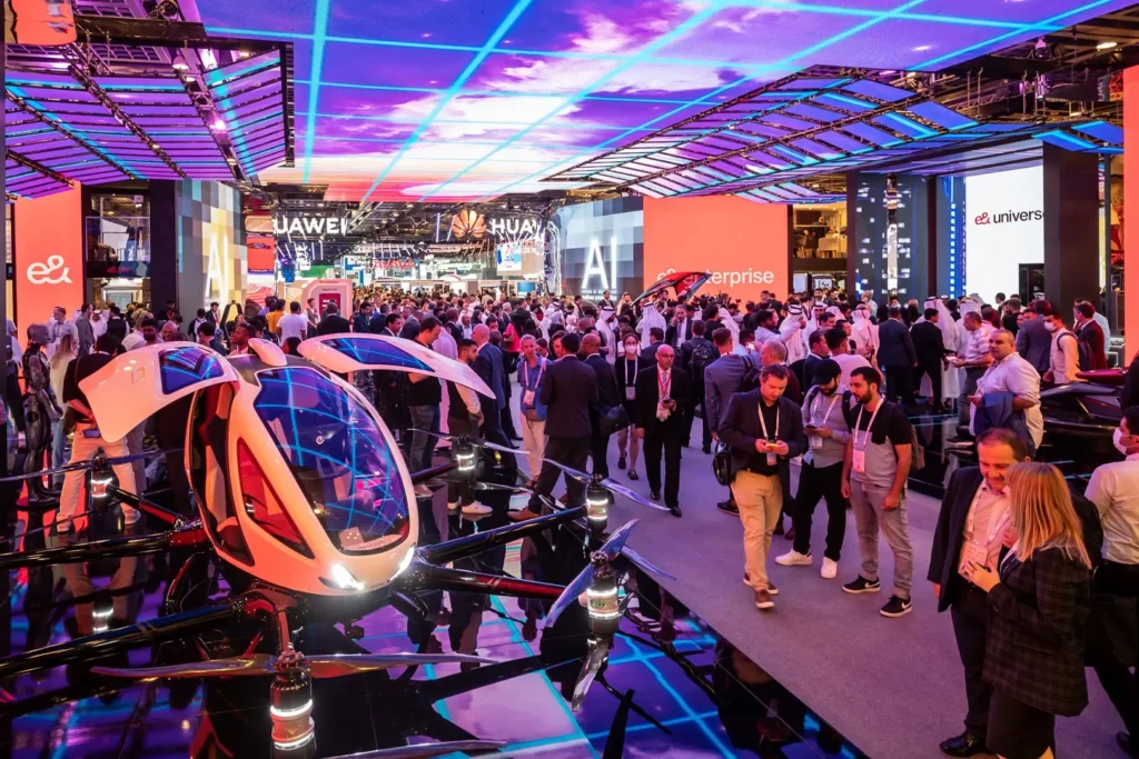 A busy exhibition floor with attendees walking past an experimental aerial transport vehicle.