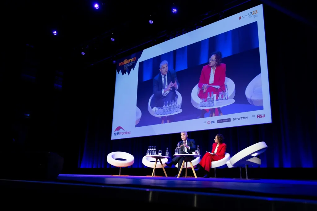 Two health sector leaders speak on stage during a conference discussion.
