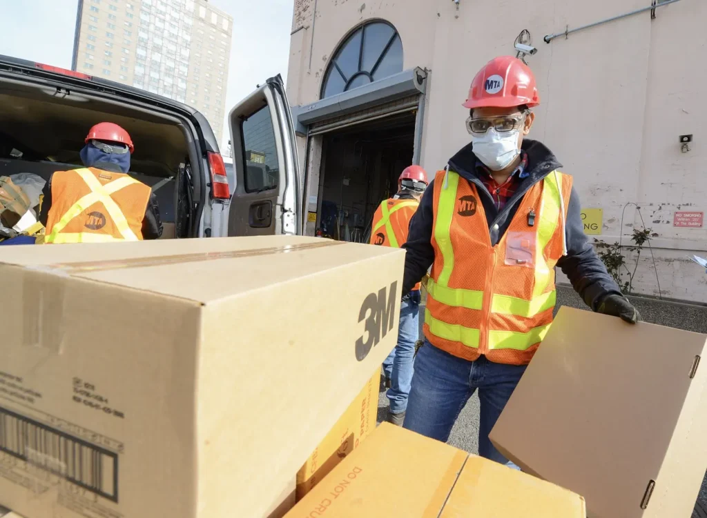 Workers in bright protective gear handling some boxes.