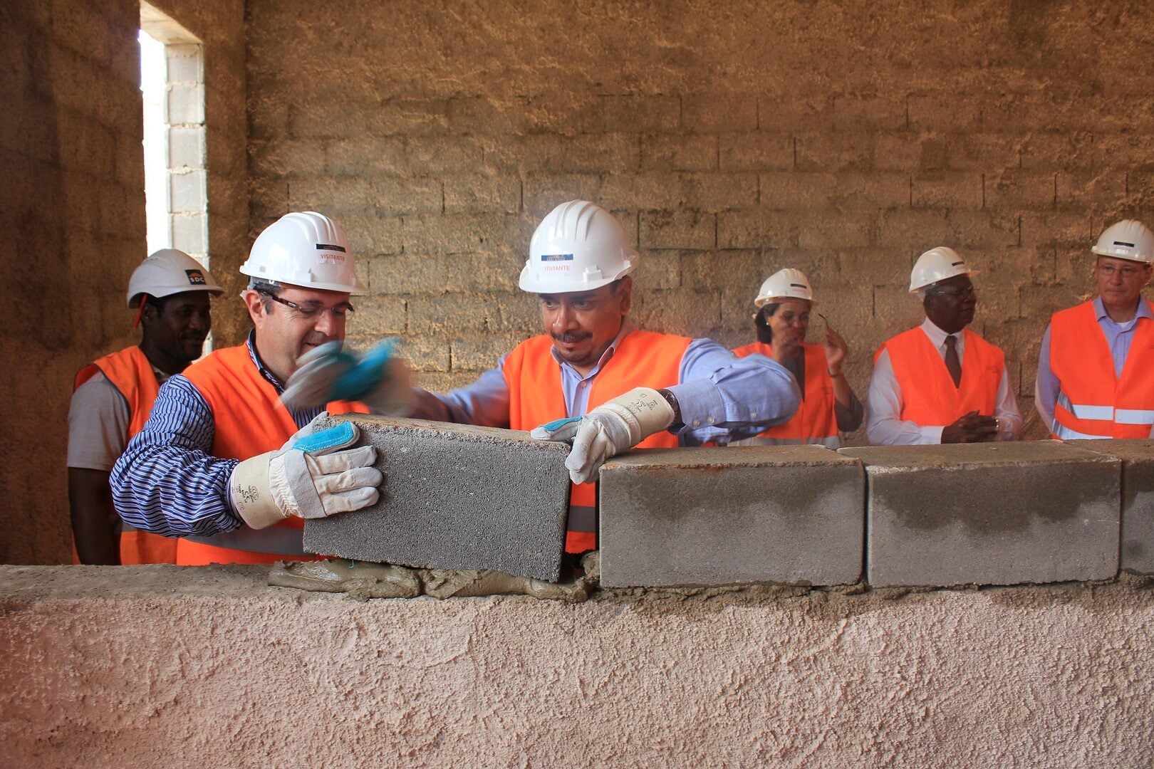 A group of workers wearing helmets and vests holding a block.