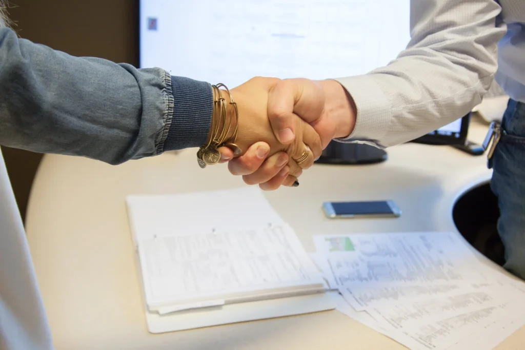 A lady wearing wrist bangles shakes another person's hand.
