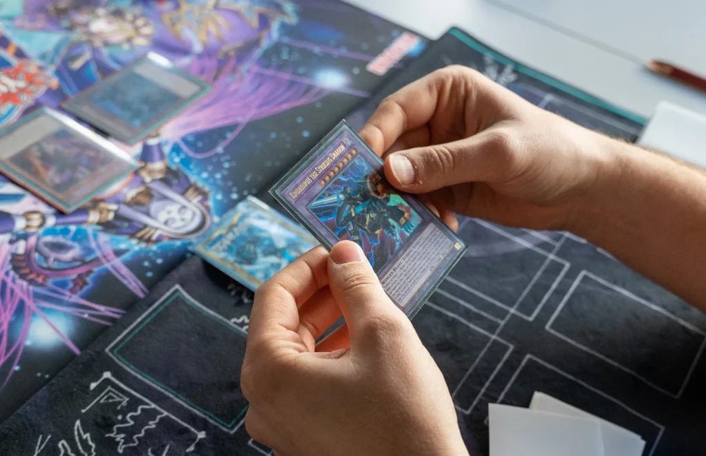 A person holding a Magic: The Gathering card with both hands above a play mat. 