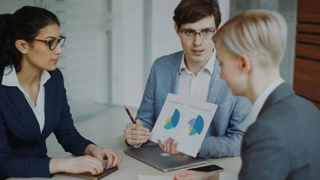 Three workers inspect two pie graphs.