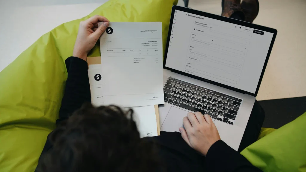 A person inspection an invoice while working on their laptop.