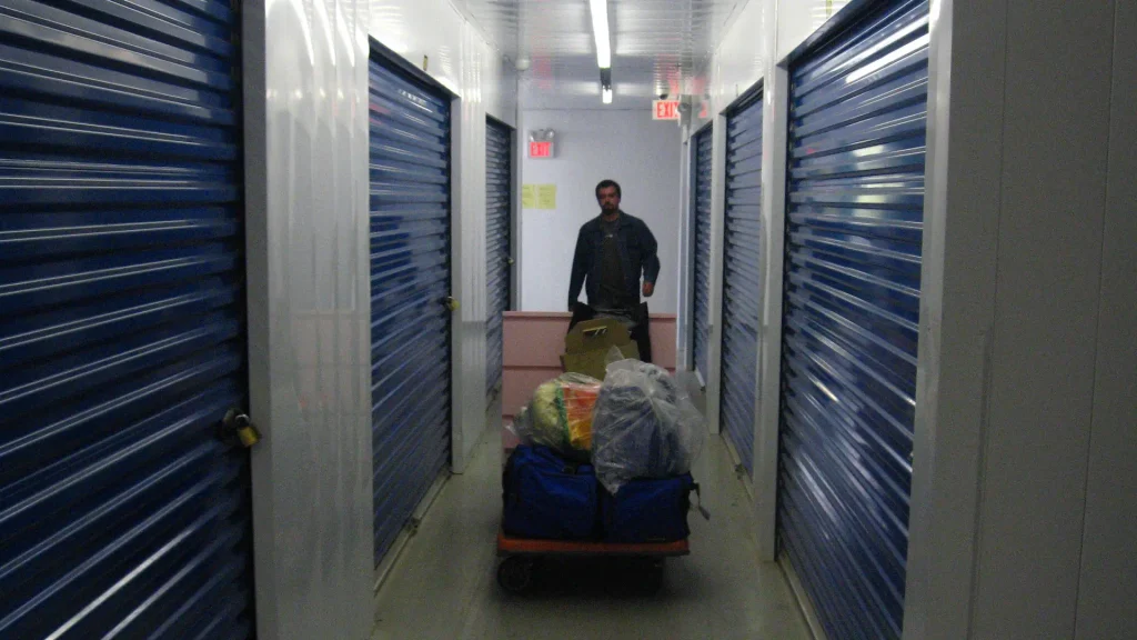 A man with items in a storage unit facility hallway.